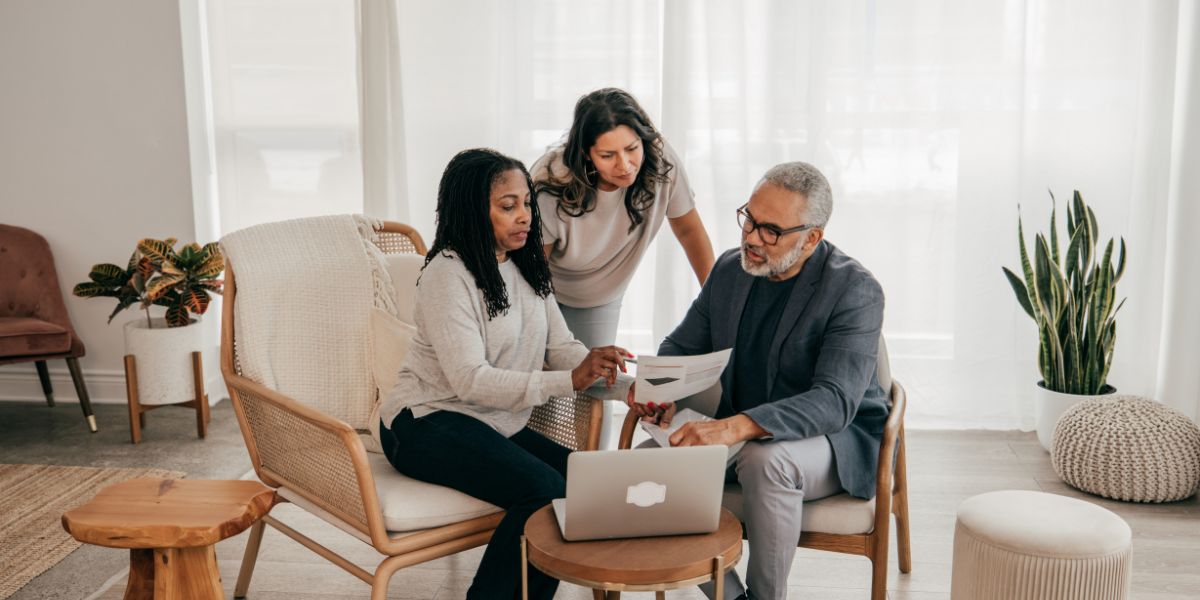 Three people reviewing documents deciding whether to buy or rent together in a modern living room.