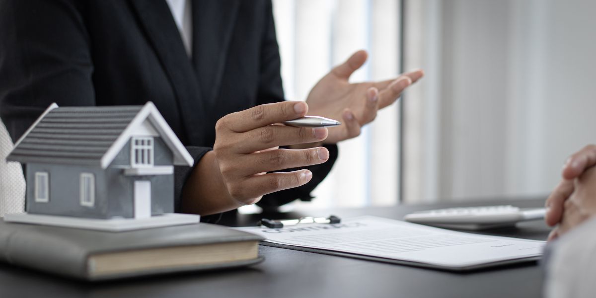Home insurance agent discussing policy details with a small house model on the desk.