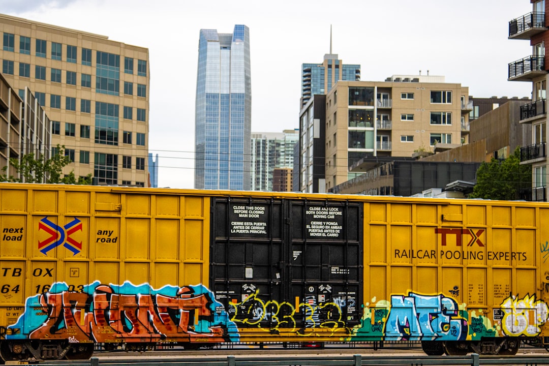 Professional movers load boxes and furniture onto a moving truck with the Denver, Colorado city skyline or mountains visible in the background.