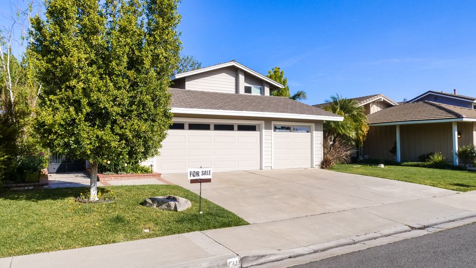 A modern 'For Sale' sign placed in the manicured front yard of an attractive suburban home, indicating the process of selling a property.